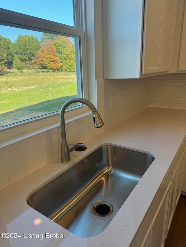 interior details featuring decorative backsplash, sink, and white cabinets