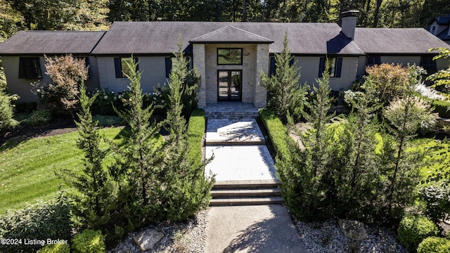 view of front facade with french doors, a chimney, a shingled roof, and brick siding