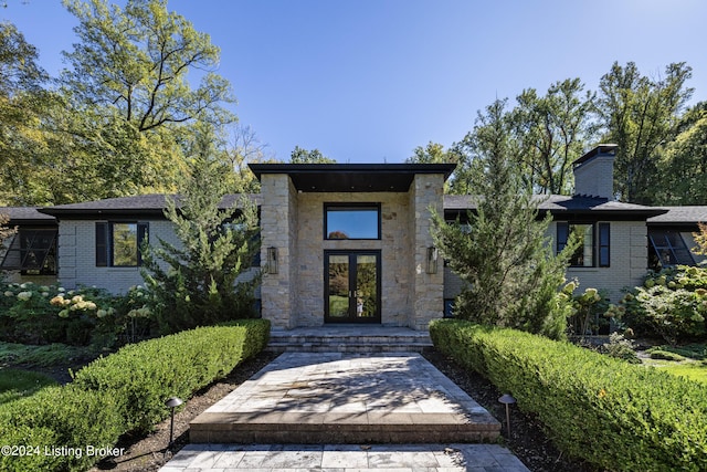 view of exterior entry featuring french doors, a chimney, and brick siding