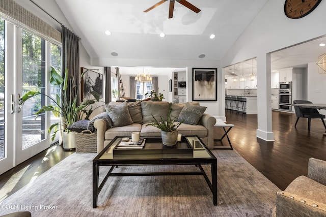 living room with high vaulted ceiling, recessed lighting, ceiling fan with notable chandelier, dark wood finished floors, and decorative columns