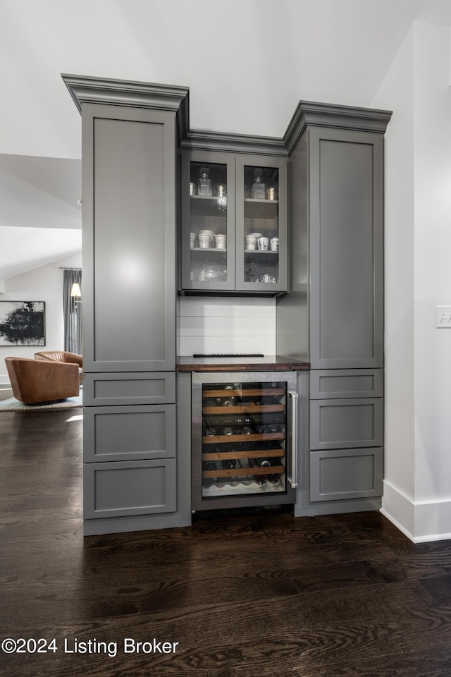 bar with wine cooler, baseboards, vaulted ceiling, dark wood-style floors, and a dry bar