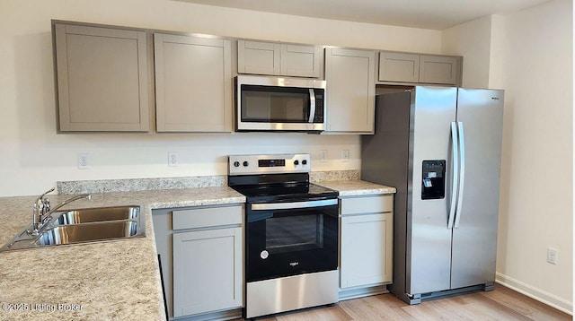 kitchen with a sink, stainless steel appliances, light wood-style floors, and gray cabinetry