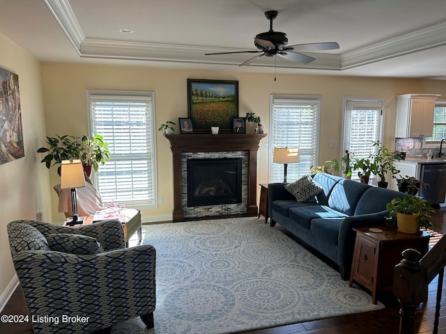 living room featuring ceiling fan, crown molding, hardwood / wood-style floors, a raised ceiling, and a fireplace