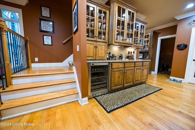 bar with beverage cooler, tasteful backsplash, light stone counters, crown molding, and light hardwood / wood-style floors