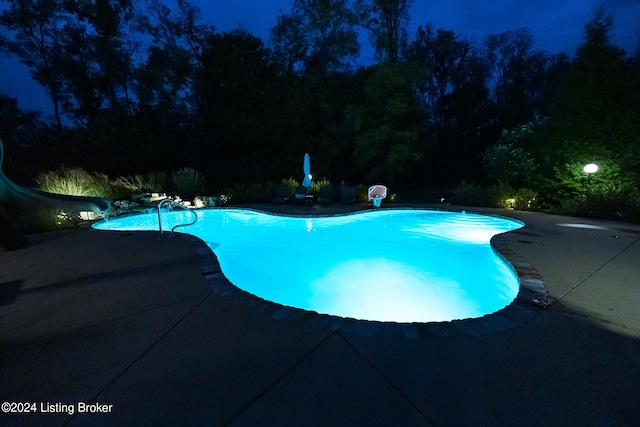 pool at night with a patio and a water slide