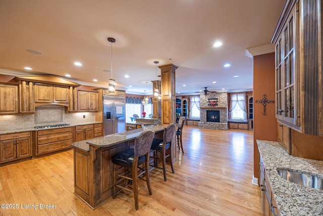 kitchen with a kitchen bar, appliances with stainless steel finishes, crown molding, decorative light fixtures, and a stone fireplace