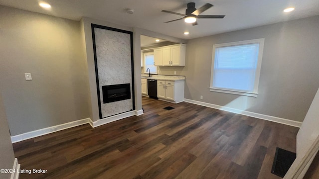 unfurnished living room featuring ceiling fan, sink, a premium fireplace, and dark wood-type flooring