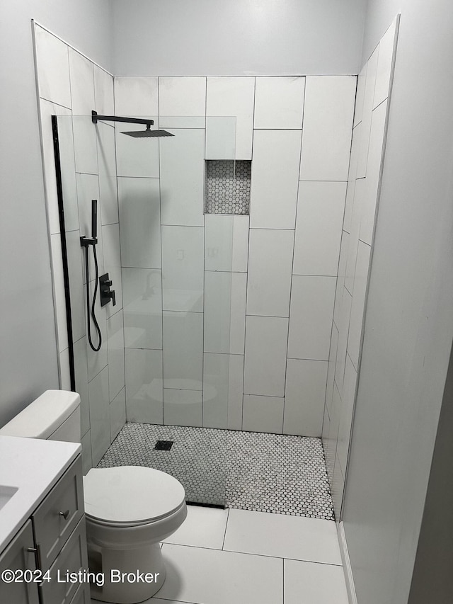 bathroom featuring tile patterned flooring, tiled shower, vanity, and toilet