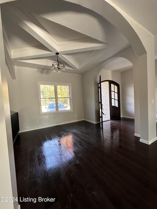 spare room with an inviting chandelier, beamed ceiling, and dark hardwood / wood-style floors