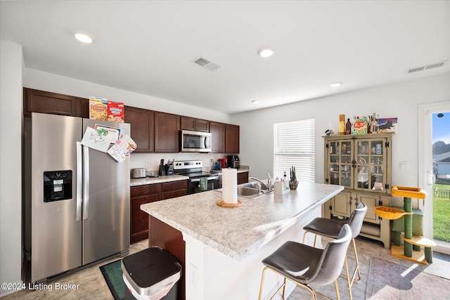 kitchen featuring dark brown cabinetry, sink, a breakfast bar area, appliances with stainless steel finishes, and a center island with sink