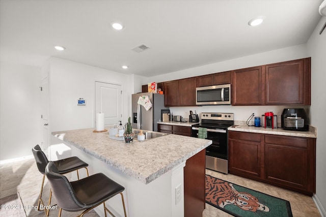 kitchen with stainless steel appliances, a breakfast bar area, a center island with sink, and dark brown cabinets