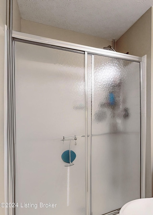 bathroom featuring walk in shower, a textured ceiling, and toilet