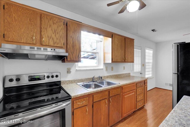 kitchen with light wood-type flooring, ceiling fan, range hood, sink, and stainless steel appliances