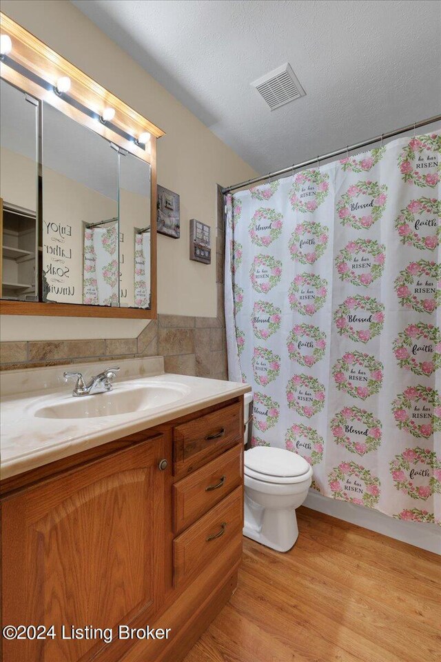 bathroom featuring a shower with curtain, vanity, wood-type flooring, toilet, and a textured ceiling