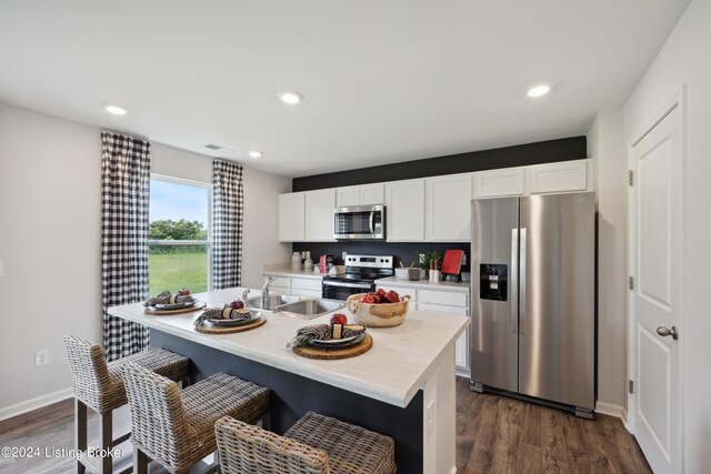 kitchen with a breakfast bar area, dark hardwood / wood-style floors, appliances with stainless steel finishes, an island with sink, and white cabinetry