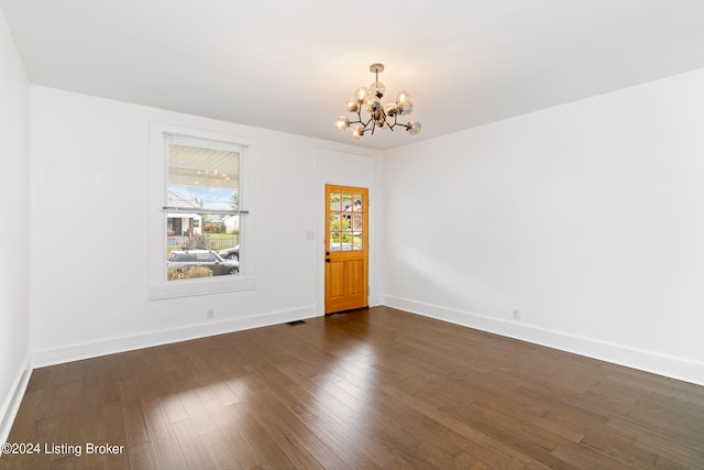 spare room with an inviting chandelier and dark hardwood / wood-style flooring