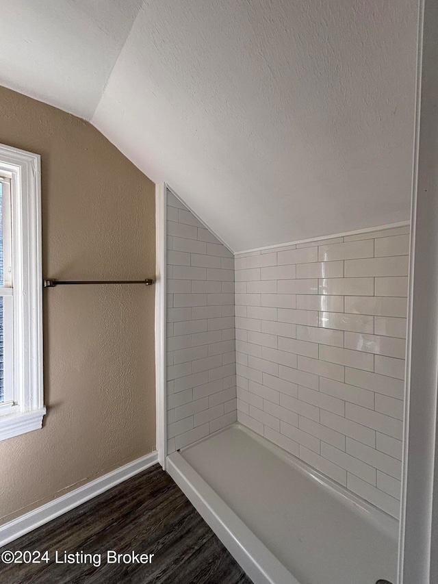 bathroom with lofted ceiling, wood-type flooring, tiled shower, and a textured ceiling