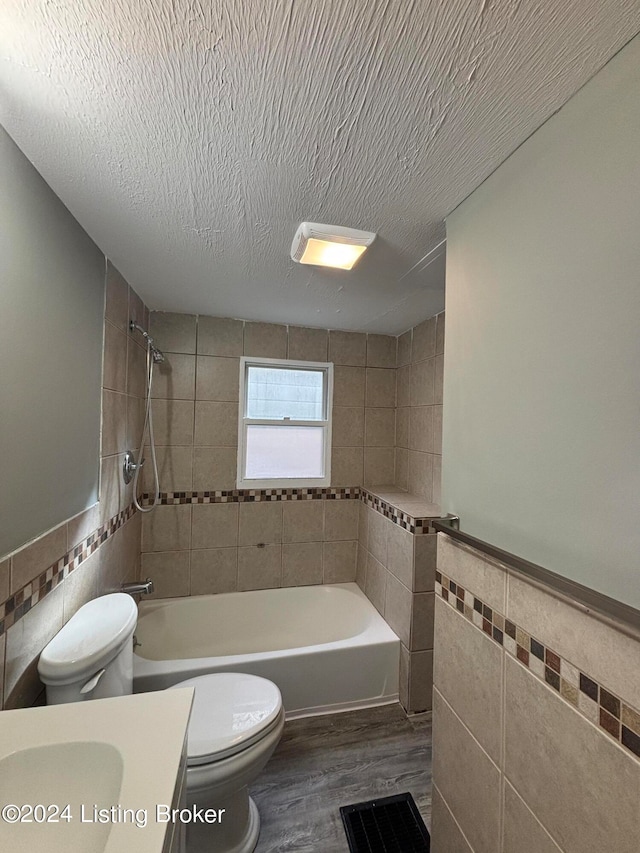 full bathroom featuring hardwood / wood-style floors, vanity, tiled shower / bath, tile walls, and toilet