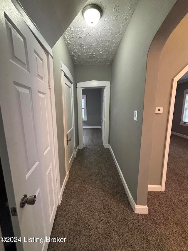 corridor with dark carpet, a textured ceiling, and a healthy amount of sunlight