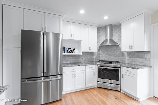 kitchen with white cabinetry, light stone countertops, wall chimney exhaust hood, light hardwood / wood-style flooring, and appliances with stainless steel finishes