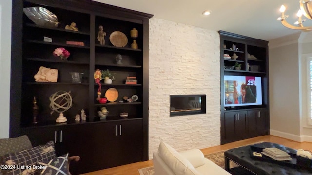 living room featuring built in shelves, a notable chandelier, a fireplace, and hardwood / wood-style floors