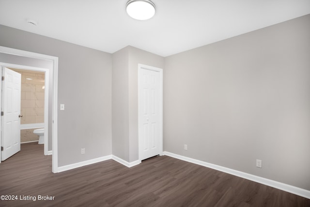 unfurnished bedroom with a closet, ensuite bathroom, and dark wood-type flooring