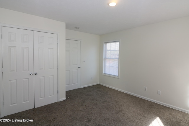 unfurnished bedroom with dark colored carpet and a closet