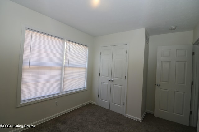 unfurnished bedroom with a closet, multiple windows, and dark colored carpet