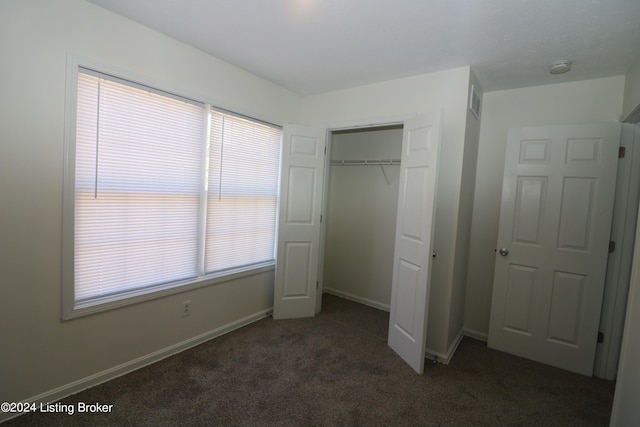 unfurnished bedroom with a closet and dark colored carpet