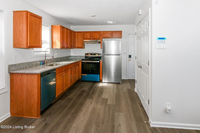 kitchen with appliances with stainless steel finishes, light stone counters, dark wood-type flooring, and sink