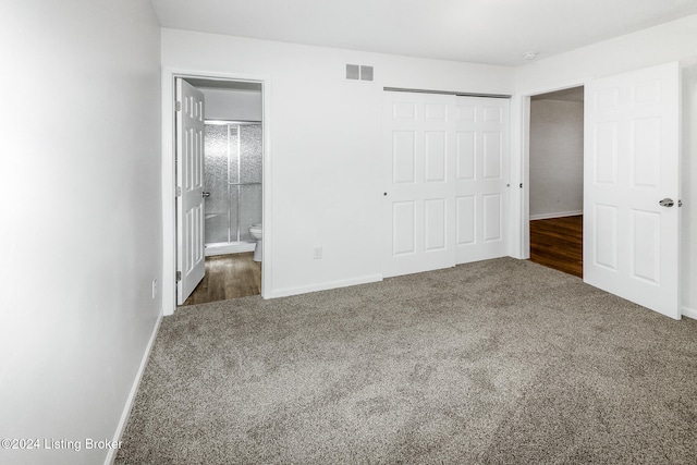 unfurnished bedroom with ensuite bathroom, dark carpet, and a closet