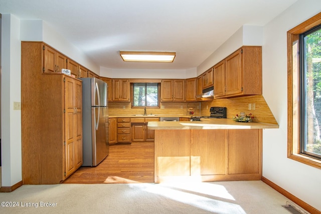 kitchen featuring tasteful backsplash, kitchen peninsula, stainless steel refrigerator, and black range oven