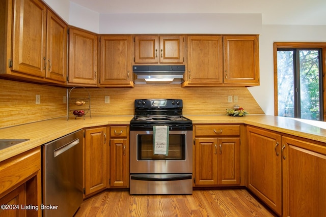 kitchen with appliances with stainless steel finishes, backsplash, kitchen peninsula, and light hardwood / wood-style flooring