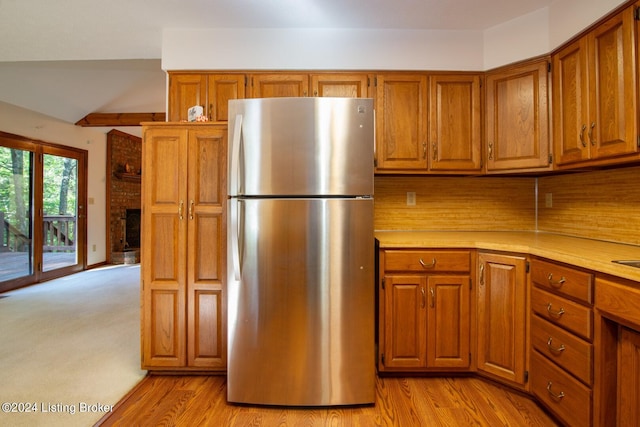 kitchen with backsplash, stainless steel refrigerator, light hardwood / wood-style flooring, and a fireplace