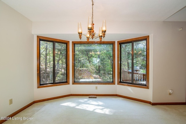 carpeted empty room featuring plenty of natural light and a chandelier