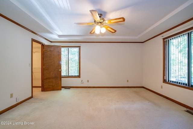 unfurnished room featuring light carpet, a tray ceiling, crown molding, and ceiling fan