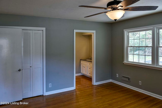 unfurnished bedroom featuring ceiling fan, dark wood-type flooring, ensuite bath, and a closet