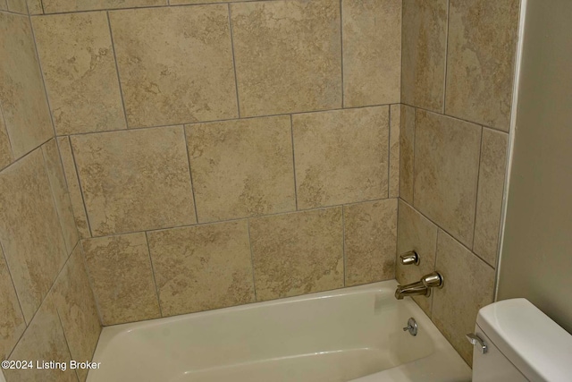 interior details featuring tiled shower / bath combo and toilet