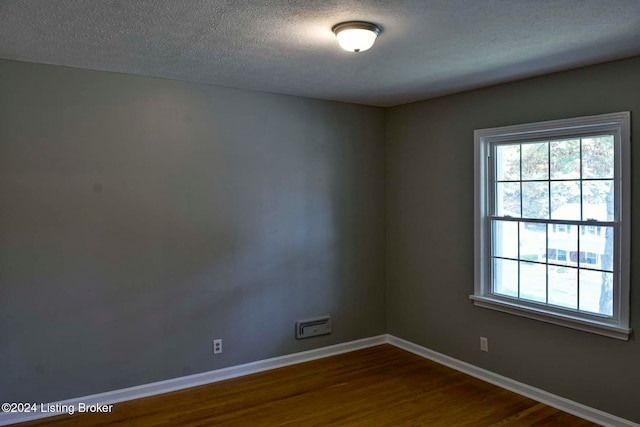 spare room with a textured ceiling, wood-type flooring, and a healthy amount of sunlight