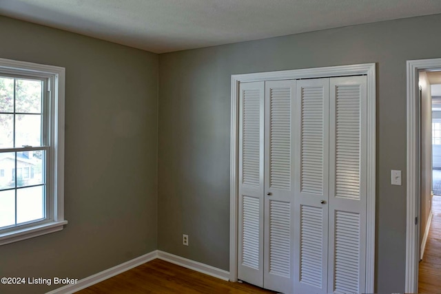 unfurnished bedroom featuring multiple windows, wood-type flooring, and a closet