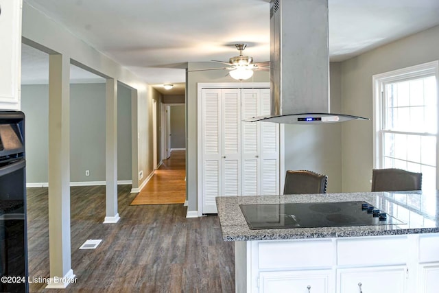 kitchen with dark wood-type flooring, dark stone countertops, black appliances, white cabinets, and island exhaust hood