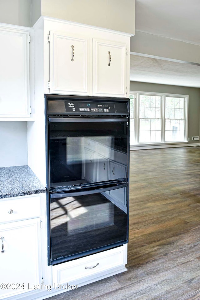 kitchen with dark stone countertops, double oven, wood-type flooring, and white cabinets