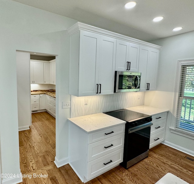 kitchen with black / electric stove, white cabinetry, tasteful backsplash, and light hardwood / wood-style flooring