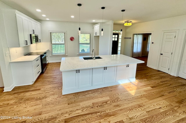 kitchen featuring sink, decorative light fixtures, appliances with stainless steel finishes, a kitchen island with sink, and white cabinets