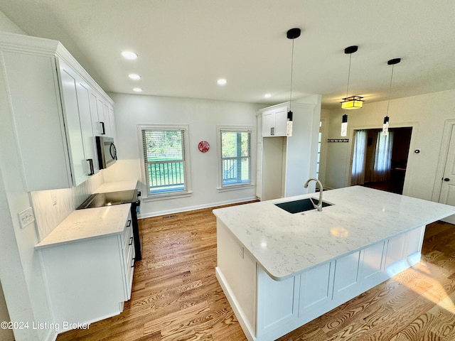 kitchen featuring pendant lighting, sink, white cabinetry, and an island with sink