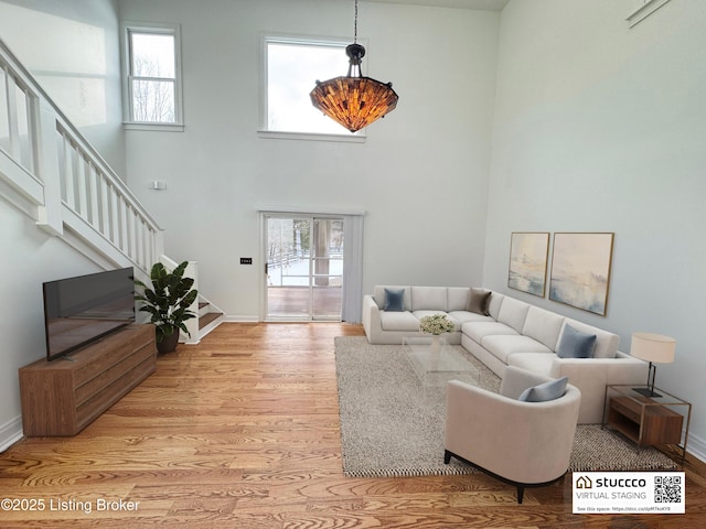 living room featuring a towering ceiling, a healthy amount of sunlight, and light wood-type flooring