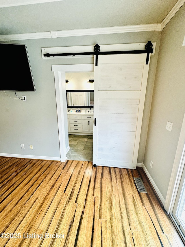 unfurnished bedroom with crown molding, a barn door, and light hardwood / wood-style flooring