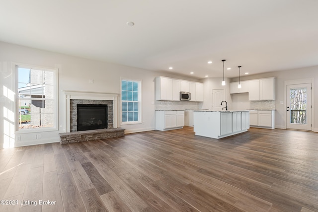 kitchen with a center island with sink, white cabinetry, tasteful backsplash, wood-type flooring, and pendant lighting