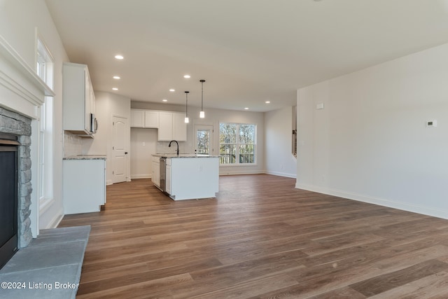 kitchen with white cabinetry, a fireplace, hanging light fixtures, hardwood / wood-style floors, and a kitchen island with sink