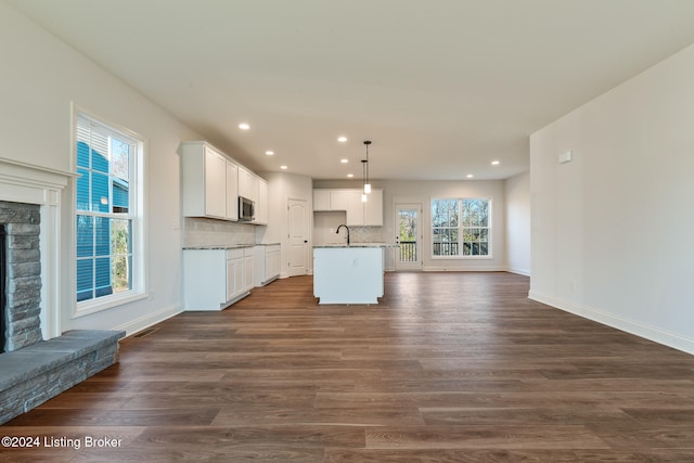 kitchen featuring dark hardwood / wood-style floors, decorative light fixtures, a fireplace, an island with sink, and white cabinets